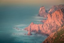 Desde arriba vista del agua de mar salpicando cerca de las rocas del Cabo Roca ubicado en el Parque Natural de Sintra Cascais al amanecer en Portugal - foto de stock
