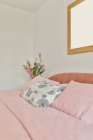 Home interior design of spacious bedroom with white walls and wooden floor furnished with comfortable bed with pink coverlet and pillows and decorated with flowers and mockup picture in daylight — Stock Photo