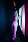Vue arrière de la jeune femme sensuelle en pantalon avec ballon regardant la caméra sur l'épaule contre les lampes au néon — Photo de stock