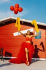 Femme noire tendance avec des numéros décoratifs et des ballons rouges debout sur la passerelle contre la construction pendant la fête d'anniversaire en plein soleil — Photo de stock