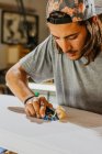 Konzentrierte männliche Meister mit Handhobel und Gestaltung glatte Oberfläche des Surfbretts in der Werkstatt — Stockfoto