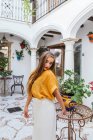 Anmutige Frau in stylischer Sommerkleidung steht neben Tisch mit Blumen im Innenhof des Hauses — Stockfoto