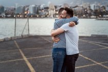 Sincero homem abraçando parceiro homossexual irreconhecível enquanto olha para longe contra o lago e montar na cidade — Fotografia de Stock