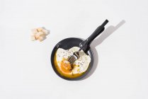 Кусочки хлеба подаются на белом столе с аппетитным жареным яйцом на сковороде с вилкой — стоковое фото