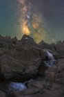 Spettacolare vista di alti monti grezzi con cascata e fiume sotto il cielo stellato con galassia in serata — Foto stock