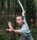 Uomo in abiti tradizionali praticare posizione spada durante la formazione di kung fu nella foresta — Foto stock