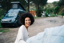 Smiling African American woman holding hands of cropped boyfriend holding hands while strolling and looking away against camper — Stock Photo