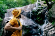 Seitenansicht eines nicht wiederzuerkennenden männlichen Wanderers, der auf einem Felsbrocken steht und den Wasserfall im Wald bewundert — Stockfoto