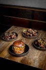 Зверху смачний бургер зі смаженими булочками, розміщеними біля тарілок з курячими крильцями в соусі барбекю в ресторані — стокове фото