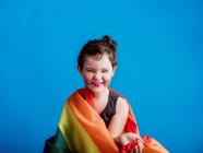 Fille souriante avec joue peinte avec drapeau multicolore sur fond bleu vif — Photo de stock