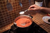 Сверху урожая женщина добавляет соль в кастрюлю во время приготовления соуса маринара из помидоров на плите на кухне — стоковое фото