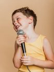 Cooles Kind beim Singen in modernem Mikrofon auf braunem Hintergrund im Studio — Stockfoto