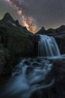 Magnífica paisagem de espuma salpicando cachoeira fluindo entre terreno rochoso áspero sob céu estrelado noite com brilhante brilhante Via Láctea — Fotografia de Stock