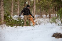 Чоловік власник в верхньому одязі грає з енергійною собакою під час прогулянки в засніженому лісі взимку — стокове фото