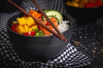 Hohe Winkel der asiatischen Poke mit Lachs und Reis mit verschiedenen Gemüse serviert in Schüssel auf dem Tisch mit Essstäbchen im Restaurant — Stockfoto