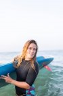 Femme en maillot de bain debout avec SUP board dans l'eau de mer en été et regardant ailleurs — Photo de stock
