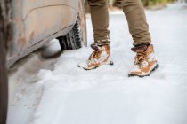 Анонімний чоловік у теплий одяг виходить з машини, припаркованої на сніговій дорозі в зимовому лісі — стокове фото