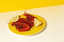 Вкусные морепродукты из приготовленных красных креветок со свежими ломтиками лимона и грубой солью на двухцветном фоне — стоковое фото