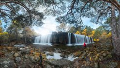 Panoramic view of traveling male in warm clothes standing and admiring view of rapid waterfall in long exposure at Lozoya river in Guadarrama National Park — Stock Photo
