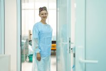 Fröhliche erwachsene Sanitäterin mit steriler Maske und Zierkappe blickt im Krankenhaus in die Kamera — Stockfoto