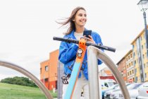 Под контентом женщины арендуют припаркованный электрический скутер в городе и просматривают мобильный телефон — стоковое фото