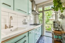 Інтер'єр сучасної кухні з бірюзовими меблями і дверима відкрився на балконі в сонячний літній день — стокове фото