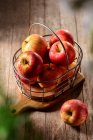 De arriba de las manzanas sabrosas maduras en la cesta metálica a la tabla de cortar en el campo en el día soleado - foto de stock