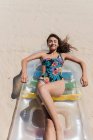De cima fêmea feliz em maiô deitado no colchão inflável na praia de areia e banhos de sol no dia ensolarado durante as férias de verão — Fotografia de Stock