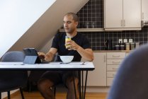 Konzentrierter Mann surft auf Tablet im Internet, während er zu Hause am Tisch sitzt und morgens frühstückt — Stockfoto