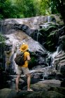 Вид сбоку на неузнаваемого мужчину-туриста, стоящего на валуне и любующегося водопадом в лесу — стоковое фото