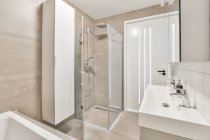 Interior del cuarto de baño con espejo colgando sobre lavabo doble colocado cerca de la puerta de entrada y cabina de ducha de vidrio en apartamento moderno - foto de stock