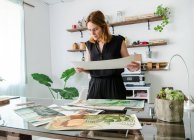 Diseñadora femenina creativa examinando varias pinturas colocadas en la mesa y trabajando en el proyecto - foto de stock