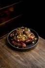 Сверху вкусные жареные куриные крылышки в соусе барбекю, украшенном свежими овощами, подаваемые на тарелке на деревянном столе в ресторане — стоковое фото
