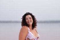 Зачарована пишна жінка в бікіні стоїть біля води рожевого ставка влітку і дивиться на камеру — стокове фото