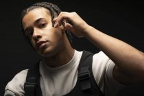 Handsome young ethnic male with Afro braids dressed in black and white clothes looking at camera while sitting in dark studio — Stock Photo