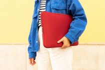 Cropped unrecognizable female freelancer with netbook in red case standing in city street — Stock Photo