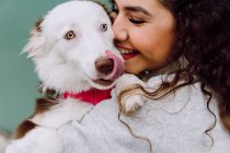 Encantada propietaria femenina abrazando al lindo perro Border Collie y sonriendo con los ojos cerrados sobre fondo azul - foto de stock