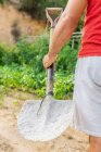 Back view of crop anonymous male farmer with shovel standing in field on farm in summer — Stock Photo