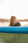 Female surfer lying on SUP board and floating on calm water of sea on sunny day looking away during sunset — Stock Photo