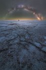 Далекий силует дослідника стоїть і тримає ліхтарик у сухій солоній лагуні на тлі зоряного неба з сяючим Молочним Шляхом вночі. — стокове фото