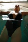 Giovane bella donna sdraiata sul marciapiede della piscina coperta, indossando costume da bagno nero — Foto stock