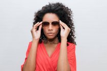 Trendige junge Afroamerikanerin mit lockigem Haar in roter Kleidung und Sonnenbrille blickt in die Kamera — Stockfoto