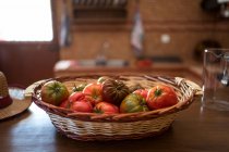 Pilha de tomates frescos em cesta de vime colocada na mesa na cozinha rústica na época da colheita — Fotografia de Stock