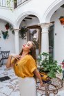 Изящная женщина в стильной летней одежде стоит у стола с цветами во внутреннем дворике дома — стоковое фото