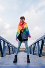 Von unten steht ein homosexueller Mann mit Regenbogenfahne auf einer Brücke und blickt in die Kamera — Stockfoto