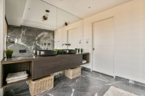 Стильний дизайн інтер'єру розкішної просторої ванної кімнати з мармуровою плиткою, обставленою подвійним умивальником і темно-коричневим дерев'яним шафою під великим дзеркалом в сучасній квартирі — стокове фото