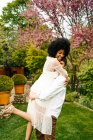 Side view of man lifting black woman while standing on meadow in garden — Stock Photo