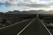Geradlinige Asphaltstraße durch Feld in Richtung Bergfahrt am Morgen auf Fuerteventura, Spanien — Stockfoto