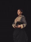 Selbstbewusste erwachsene Afroamerikanerin in eleganter Jacke blickt in die Kamera im dunklen Studio auf schwarzem Hintergrund — Stockfoto