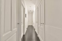 Перспективный вид на пустой узкий коридор с белыми дверями и стенами в современной квартире — стоковое фото